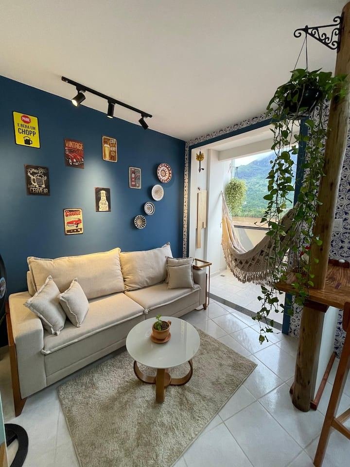 Sala do flat com sofá, varanda, rede e vista para o Pico da Ibituruna